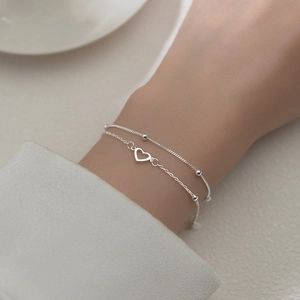 Close-up of double-layer silver bracelet featuring hollow heart charm on wrist