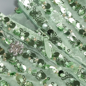 Detail of light green sequin dress showing invisible zipper and rhinestone flower