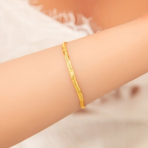 Detailed view of an 18k gold plated herringbone snake chain bracelet worn on a wrist