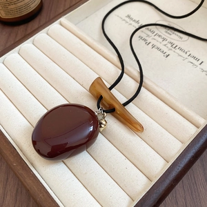 Detailed shot of vintage necklace with deep red stone pendant and small golden acorn charm