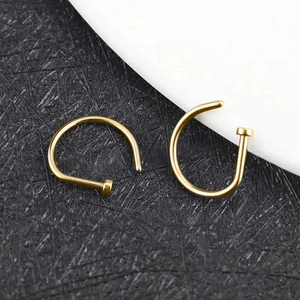 Macro shot of two golden D-shaped nose rings and curved barbells on a dark background