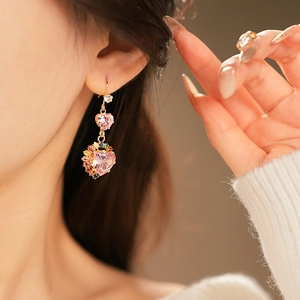 Close-up of golden drop earrings with colorful heart-shaped stones worn by a model
