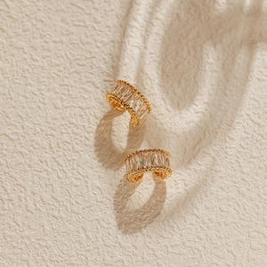 Detailed close-up of C-shaped 18K gold plated ear cuffs with baguette-cut zircons