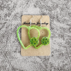 Détail de boucles d'oreilles cœur en acrylique pailleté vert avec motif pickleball