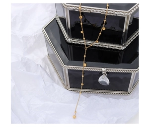 Detailed shot of long Y-shaped gold beaded necklace with a silver teardrop pendant