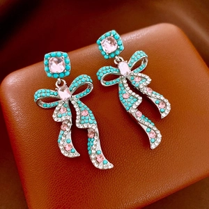 Macro detail of bow-shaped tassel earrings with pink gemstones and turquoise beads