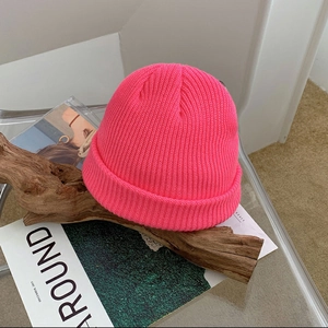 Detail of neon pink knitted beanie with ribbed texture on wooden decorative stand