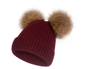 Gros plan sur la texture côtelée et les pompons en fausse fourrure brune du bonnet tricoté bordeaux
