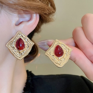 Close-up of vintage gold rhombus earrings with red water-drop gemstones and embossed patterns