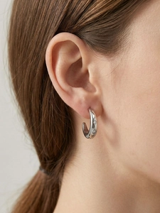 Detailaufnahme der C-förmigen 18k vergoldeten Ohrringe mit Zirkonia am Ohr des Models