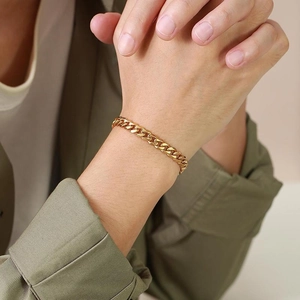 Detailed view of a gold-plated Cuban link chain bracelet worn on a wrist with a green jacket