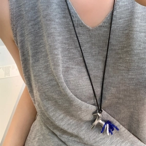 Silver metal horse pendant necklace with blue and white beads on a grey sweater