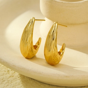 Textured gold stainless steel C-shaped teardrop stud earrings on ceramic dish