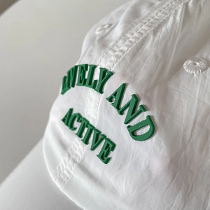 Close-up of green embossed 'LIVELY AND ACTIVE' text on white nylon baseball cap