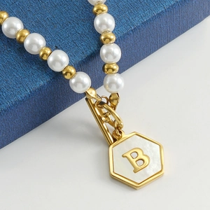 Vue macro du collier de perles avec pendentif en nacre dorée et la lettre B gravée dessus