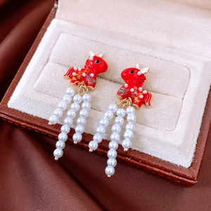 Detail of red enamel horse earrings with hanging white pearl tassels in a jewelry box