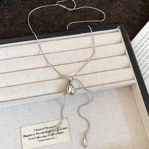 Macro detail of a silver teardrop tassel pendant necklace on a beige jewelry display tray