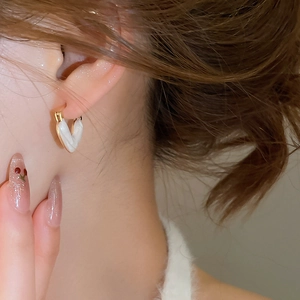 Close-up of heart-shaped white enamel earrings with golden edges on a female model
