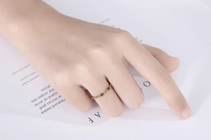 Dettaglio di un sottile anello a catena dorato con zirconi verdi indossato su un dito