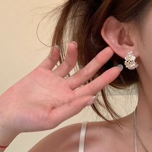 Detailed close-up showing white pearl flower C-shape stud earrings on a model ear