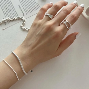 Detail of minimalist silver stackable rings and beaded bracelets on a model's hand