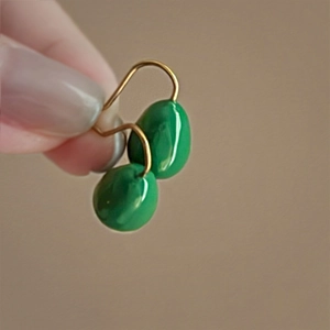 Detail of green teardrop earrings held in hand with gold hooks and polished finish