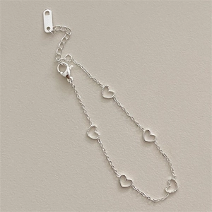 Minimalist silver 316L stainless steel bracelet with heart charms on beige background