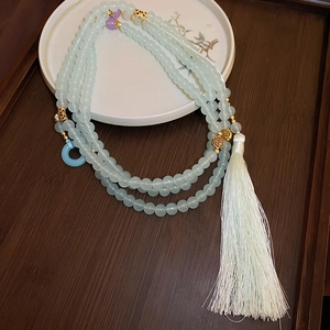 Detail of light green beaded necklace with cream tassel on a zen wood tray