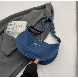 Detailed close-up of a blue denim crescent bag with metal zipper and adjustable strap
