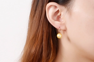 Détail de boucles d'oreilles en perles or rose portées montrant le fini brillant et chic