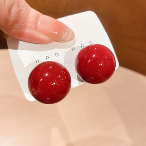 Detailed close-up of glossy red spherical stud earrings with silver pins on a card
