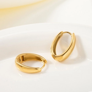 Polished 18k gold plated oval huggie hoop earrings displayed on a white ceramic tray