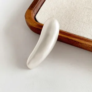 Minimalist long bar metal brooch with smooth pearl white finish shown on a wooden tray