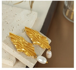 Close-up of golden leaf-shaped earrings with freshwater pearls on a stone tray