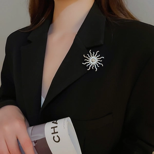 Silver sunburst brooch with pearl detail pinned on a black blazer lapel for a stylish look