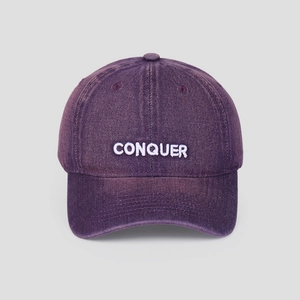 Macro detail of embroidered white CONQUER text on washed vintage denim baseball cap