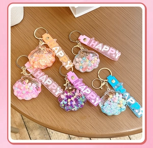 Detail of shell-shaped liquid glitter keychains with HAPPY letter straps in 5 colors