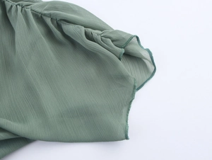 Detailansicht von salbeigrünem Chiffonstoff mit plissierter Textur und Wellensaum