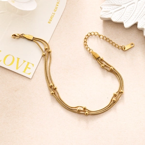 Detail of a triple-layer gold snake chain bracelet with polished metal beads and lobster clasp