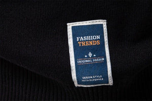 Détail de l'étiquette tissée bleue et blanche sur un pull en maille noir ajusté