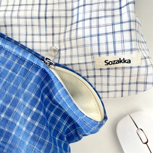 Detail of blue and white checkered cotton makeup bag with metal zipper and brand label