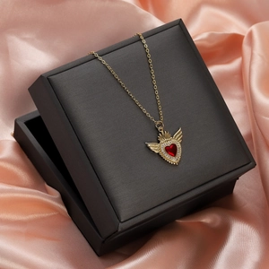 Detail of red heart necklace with gold wings in jewelry box on pink silk