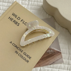 Detailed view of a medium white pearlescent hair claw clip resting on an open book
