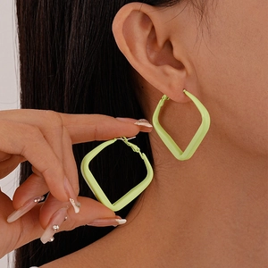 Close-up of geometric neon green diamond earrings on ear and hand for size scale