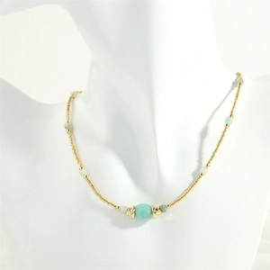Detail of beaded necklace with gold-toned accents and turquoise stone beads on a mannequin