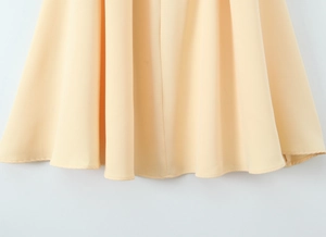 Gros plan de l'ourlet de la robe jaune clair montrant le drapé fluide et les coutures