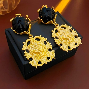 Close-up of golden irregular lion head earrings with black round studs on jewelry box