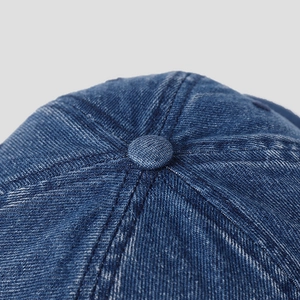 Macro detail of navy blue denim baseball cap showing top button and stitching quality