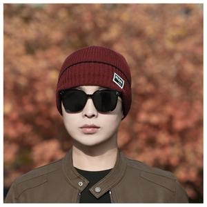 Detail of burgundy ribbed knit beanie with fashion label and black horizontal stripes
