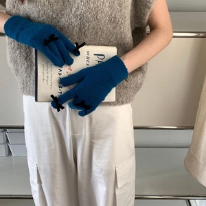 Close-up of blue knit gloves with black bow accent held against a book background